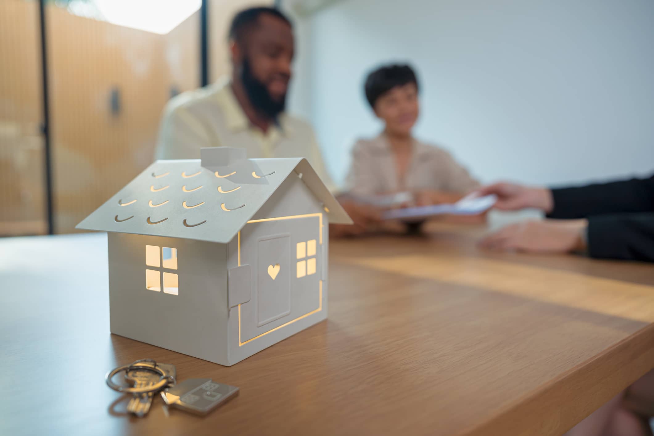 Mature couple firms the contract for buying a home. House key and tiny house on table.